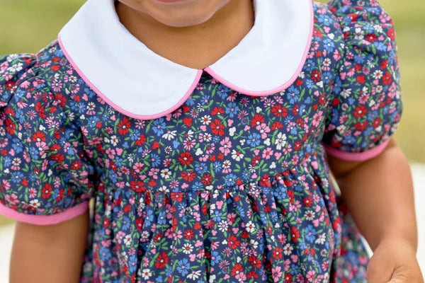 Child wearing a floral dress with a white collar against a blurred natural background