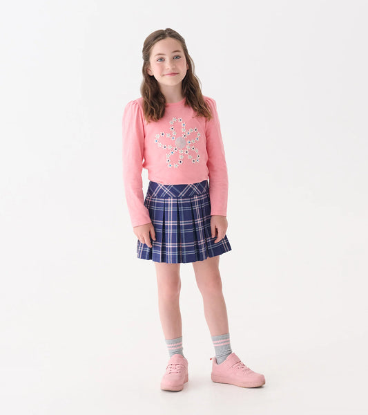 Young girl wearing a pink sweater with a snowflake design and a blue plaid skirt on a white background