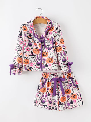 A two-piece children's pajama set featuring a long-sleeve top and matching shorts with a white background and a colorful Halloween print of pumpkins, ghosts, witches, and cauldrons. The set is accented with purple trim and purple ties, shown hanging on a wooden hanger against a plain white background.