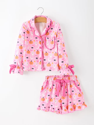 A two-piece girls' pajama set featuring a long-sleeve button-front top and matching shorts, both in pink with an all-over pumpkin, moon, and cat print. The top has a collar and bow details on the cuffs, while the shorts have an elastic waist and a side bow.