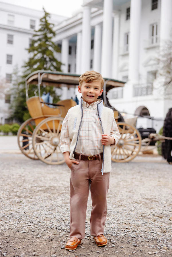 Young boy in formal attire standing in front of a classic car and building.