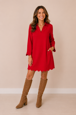 A woman modeling a bright red long-sleeve mini dress with a scalloped hem, paired with brown suede knee-high boots, against a solid beige studio background.