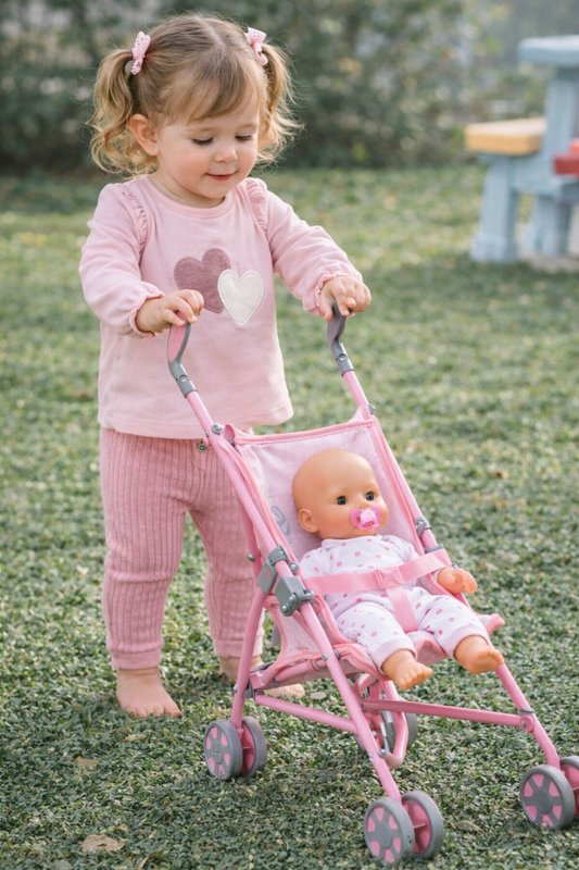Child pushing a pink stroller with a doll in it outdoors.