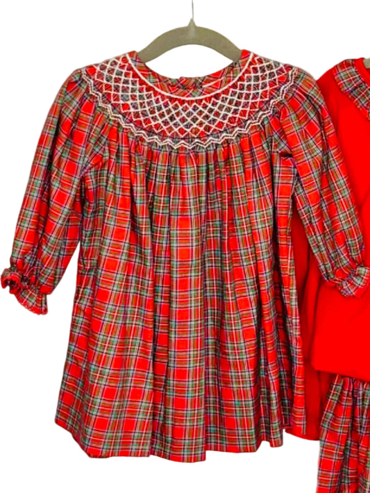 Two children's outfits on a white rack with a Christmas tree in the background.