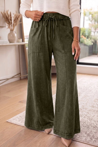 Woman wearing olive green mineral wash flared pants with a relaxed wide-leg fit and front pockets.