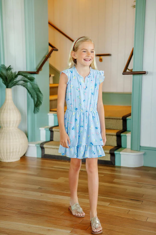 Young girl in a light blue dress standing in a home interior with wooden floor and staircase.