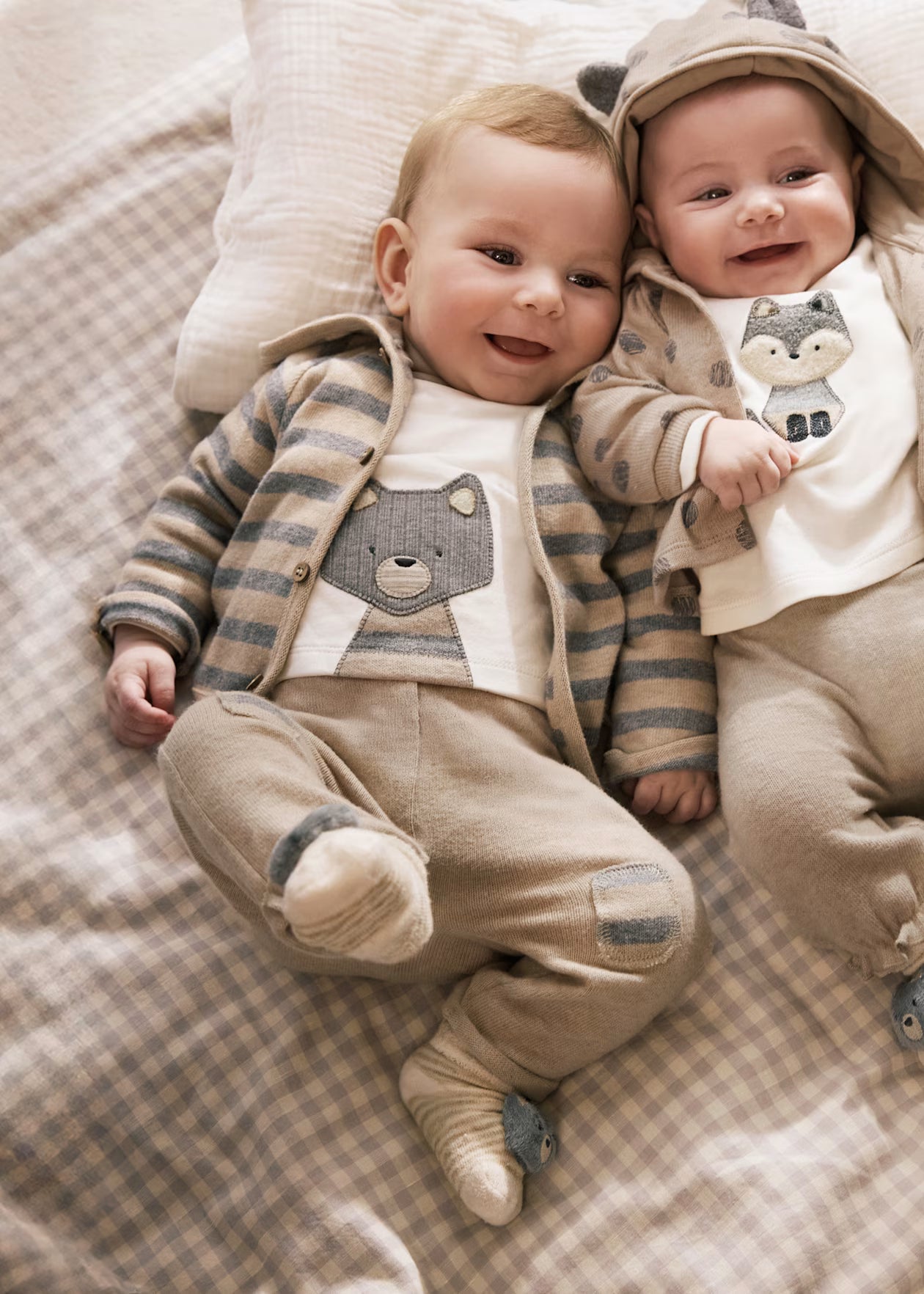 Two babies in matching outfits lying on a checkered blanket