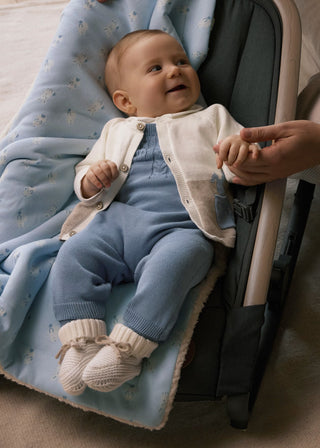 Baby in blue overalls and white sweater sitting in a stroller with a blanket.