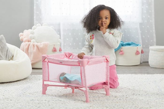 Child playing with a pink playpen in a room with soft toys and white curtains.