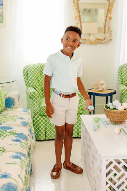 Young boy standing in a living room with green chairs and decorative items.