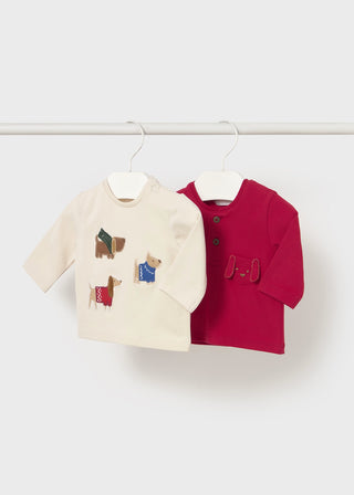 Two children's sweaters, one cream with colorful dog designs and one red, on hangers against a white background.